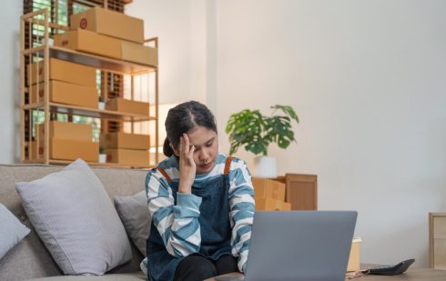 Tânără antreprenoare stresată lucrând la laptop în contextul deflației economice și problemelor financiare ale afacerii