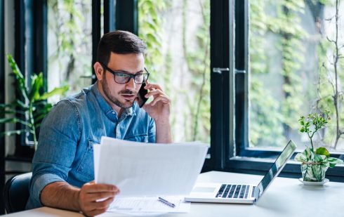 Om de afaceri analizând documente privind fideiusiunea în timp ce vorbește la telefon